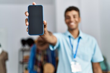 Wall Mural - Young hispanic man working as shop assistant showing phone screen at retail shop