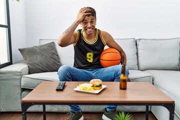 Poster - Young handsome hispanic man holding basketball ball cheering tv game stressed and frustrated with hand on head, surprised and angry face