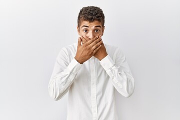 Wall Mural - Young handsome hispanic man standing over isolated background shocked covering mouth with hands for mistake. secret concept.