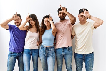 Canvas Print - Group of young people standing together over isolated background making fun of people with fingers on forehead doing loser gesture mocking and insulting.