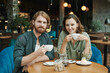 © Mediaphotos - Serious handsome guy with beard sitting at table in cafe and drinking coffee while reading mail on smartphone