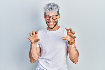 Wall Mural - Young hispanic man with modern dyed hair wearing white t shirt and glasses smiling funny doing claw gesture as cat, aggressive and sexy expression