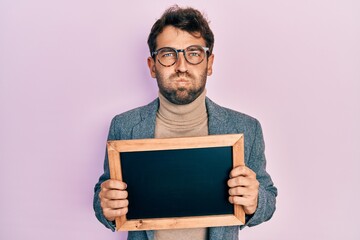 Poster - Handsome man with beard holding blackboard puffing cheeks with funny face. mouth inflated with air, catching air.