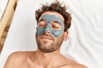 Poster - Young hispanic man having facial mask treatment at beauty center