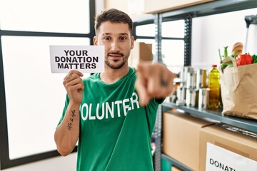 Poster - Young volunteer man holding your donation matters banner pointing with finger to the camera and to you, confident gesture looking serious