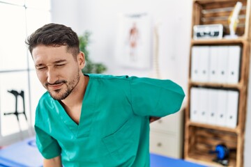 Canvas Print - Young physiotherapist man working at pain recovery clinic suffering of backache, touching back with hand, muscular pain