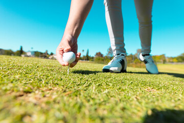 Low section of caucasian young man placing golf ball on tee over grassy land against clear blue sky