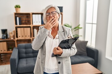 Poster - Middle age woman with grey hair at consultation office bored yawning tired covering mouth with hand. restless and sleepiness.