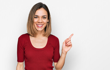 Wall Mural - Young blonde girl wearing casual clothes with a big smile on face, pointing with hand finger to the side looking at the camera.