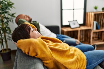 Wall Mural - Young hispanic couple smiling happy relaxed with hands on head sitting on the sofa at home.