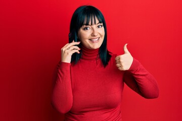 Sticker - Young hispanic woman having conversation talking on the smartphone smiling happy and positive, thumb up doing excellent and approval sign