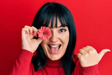 Canvas Print - Young hispanic woman holding sunflower over eye pointing thumb up to the side smiling happy with open mouth