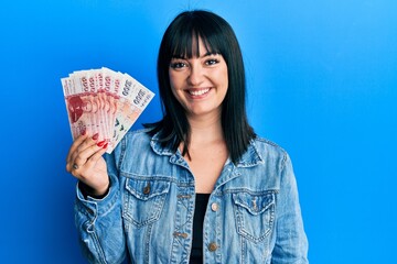 Wall Mural - Young hispanic woman holding icelandic krona banknotes looking positive and happy standing and smiling with a confident smile showing teeth