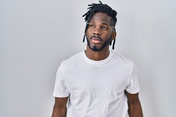 Wall Mural - African man with dreadlocks wearing casual t shirt over white background smiling looking to the side and staring away thinking.