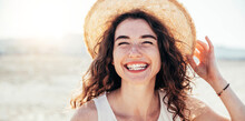 Young Joyful Woman In White Shirt Wearing Hat Smiling At Camera On The Beach - Traveler Girl Enjoying Freedom Outdoors On A Sunny Day - Wellbeing, Healthy Lifestyle And Happy People Concept