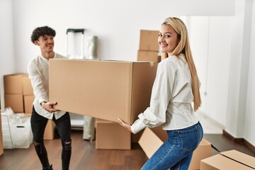 Poster - Young beautiful couple smiling happy holding big cardboard box at new home.