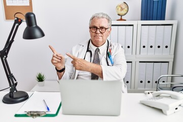 Canvas Print - Senior caucasian man wearing doctor uniform and stethoscope at the clinic pointing aside worried and nervous with both hands, concerned and surprised expression