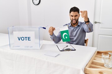 Wall Mural - Young handsome man with beard at political campaign election holding pakistan flag annoyed and frustrated shouting with anger, yelling crazy with anger and hand raised