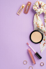 Wall Mural - Makeup concept. Top view vertical photo of stylish scarf scrunchy lip gloss compact powder gold rings and two hairpins on isolated lilac background