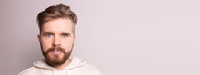 Portrait Male With Beard And Mustache And Trendy Hairdo. Wears Casual Hoodie, Has Serious Expression In Studio Against White Background Banner With Copy Space