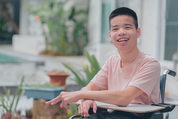 Wall Mural - Young man with disability with happy face in nature garden background of home or hospital or school or park, Teenager boy sitting with tray for activities on wheelchair, Good mental health concept.