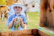 A teenage boy beekeeper in a protective suit holds a smoker in his hands. Beekeeper's tool. Inspection of wooden beehives. beekeeping. Apiary in nature.