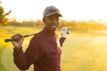 Portrait Of Smiling African American Young Man Wearing Cap With Golf Club Standing At Golf Course