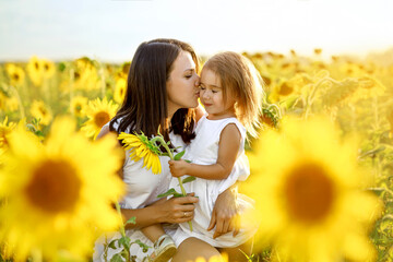 Mom gently kisses her little girl in gratitude for the gift of a sunflower flower for mother's Day. Love, affection, care and mutual understanding in the family