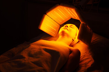 Wall Mural - An elderly woman undergoes a facial rejuvenation procedure. Woman face lt Red light treatment At beauty clinic. Cosmetology.