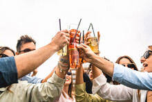 Group Of Young Friends Raises Plastic Glasses With Spritz And Fruit Cocktails For A Celebrate Toast Against A White Background Sky - Concept Of Happy People Having Fun Outdoors Drinking And Clinking
