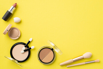 Wall Mural - Make-up concept. Top view photo of compact powder makeup brushes eyeshadow container white beauty blender blush palette and lipstick on isolated yellow background with blank space