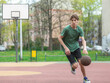 © Natali - Cute young teenager in green t shirt with a ball plays basketball on court. Sports, hobby, active lifestyle for boys