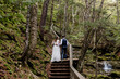 Back view of a bride and groom on a wooden stairway in a magical green forest in New Brunswick
