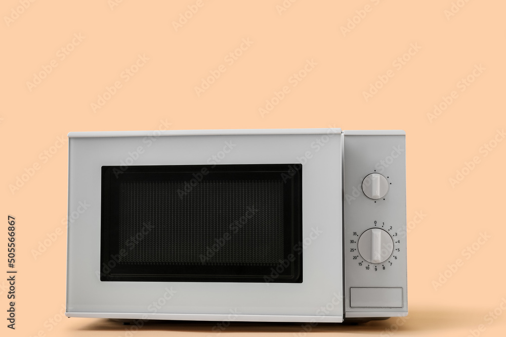 White microwave oven with opened door on beige background