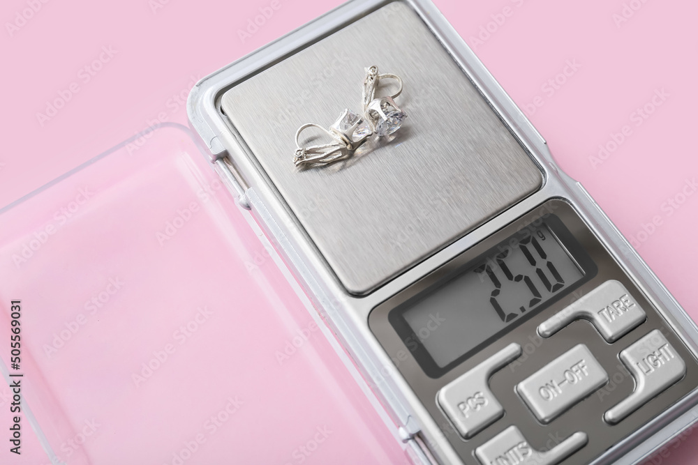 Jewelry scales with earrings on pink background, closeup