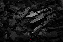 Modern Knives With Black Blades. Hunting, Military And Folding Knives On Smoldering Charcoal. Black Back.