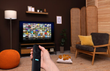 Wall Mural - Woman with remote control changing channels while watching TV at home, closeup