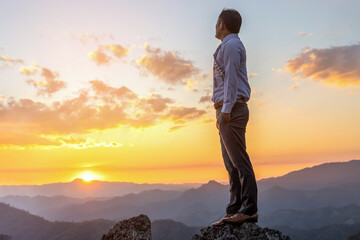 Wall Mural - Successful businessman in business suit standing and looking sunset on top rock mountain background,  competition and leadership concept.