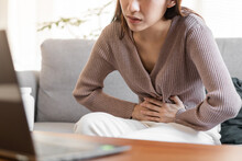 Flatulence Asian Young Woman Hand In Stomach Ache Suffer From Food Poisoning, Gastritis Or Diarrhoea, Pain Belly, Abdomen Or Inflammation, Use Laptop Computer Consulting With Doctor Online At Home.