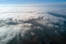 Aerial View From High Altitude Of Distant City Covered With Puffy Cumulus Clouds Flying By Before Rainstorm. Airplane Point Of View Of Landscape In Cloudy Weather