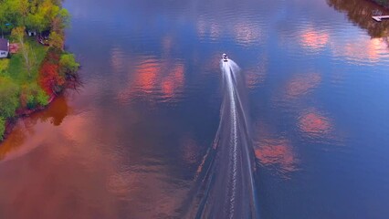 Wall Mural - Aerial view of speed boat tearing across tranquil river's surface reflecting beautiful clouds and sky.
