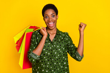 Photo of lucky excited trans human wear smart casual clothes holding bargains rising fist isolated yellow color background