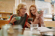 © chika_milan - Happy grandmother and her adolescent granddaughter sitting in a cafe, enjoying coffee and using smart phone for funny videos.