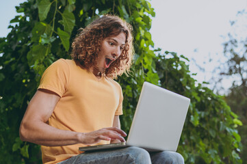 bottom view surprised shocked amazed excited young man in yellow t-shirt hold use work on laptop pc 