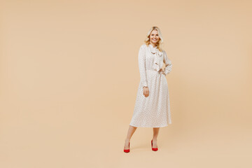 Wall Mural - Full size body length charming elderly gray-haired blonde woman lady 40s years old wears pink dress hold hand on waist looking camera posing isolated on plain pastel beige background studio portrait.