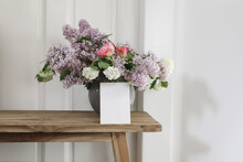 Vintage Floral Stationery Mockup. Blank Greeting Card, Invitation. Vase With Bouquet Of Lilac, Viburnum And Tulips On Old Wooden Stool. White Wooden Wall Background. Empty Copy Space.