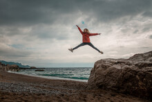 A Girl Jumps From A Stone To The Ground, Against The Background Of A Gloomy Sky On The Seashore
