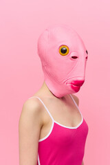Wall Mural - Funny crazy woman on a pink background standing in a fish head mask on a pink background, conceptual Halloween costume art photo