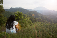 Young woman sitting alone on the ground looking at mountain range view from behind. Sad girl, healing moment. Self love and care concept. Inspirational backgrounds.