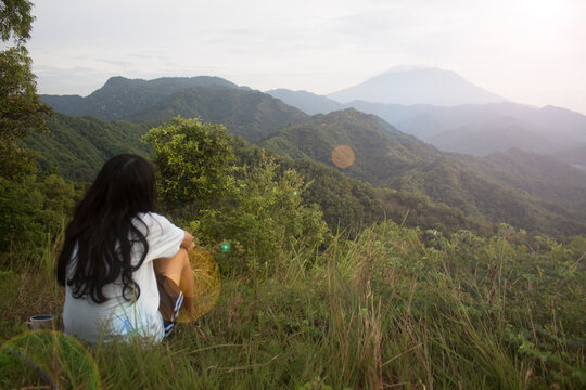 Wall Mural -  - Young woman sitting alone on the ground looking at mountain range view from behind. Sad girl, healing moment. Self love and care concept. Inspirational backgrounds.